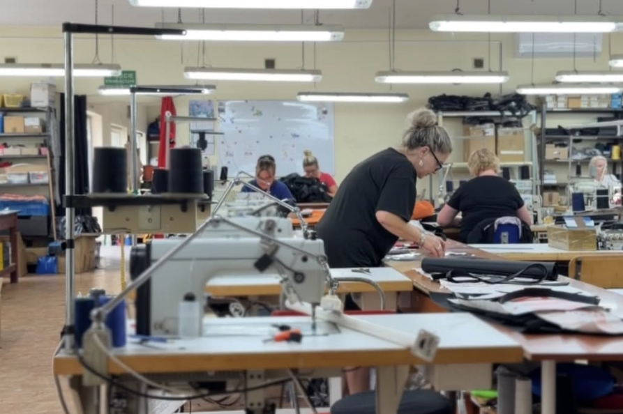 Näherin an der Industrienähmaschine in unserem Partnerwerk in Polen, im Hintergrund weitere Arbeitsplätze