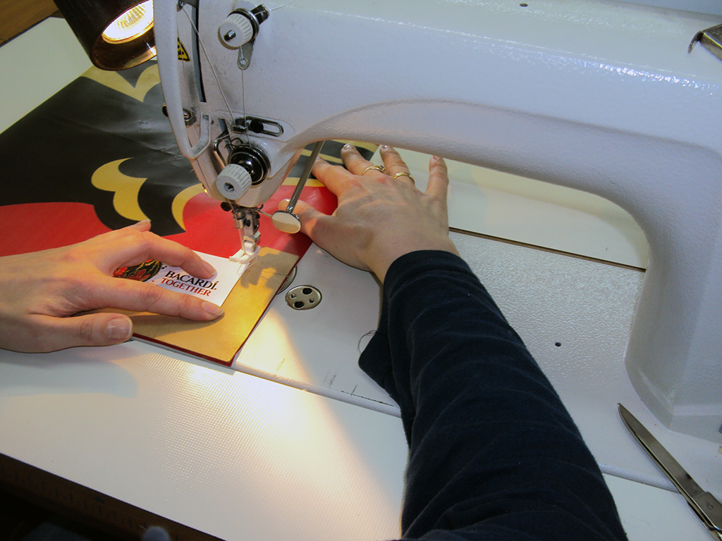 An der Nähmaschine wird ein bedrucktes Kundenlabel auf eine Tasche aus bedruckter Plane gesetzt